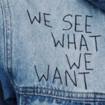 Close-up of denim jacket featuring the phrase 'We See What We Want' embroidered.